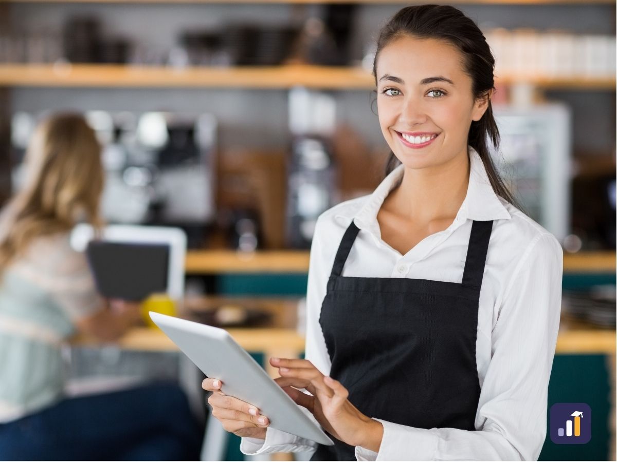Smiling cafe team member in an apron holding a tablet